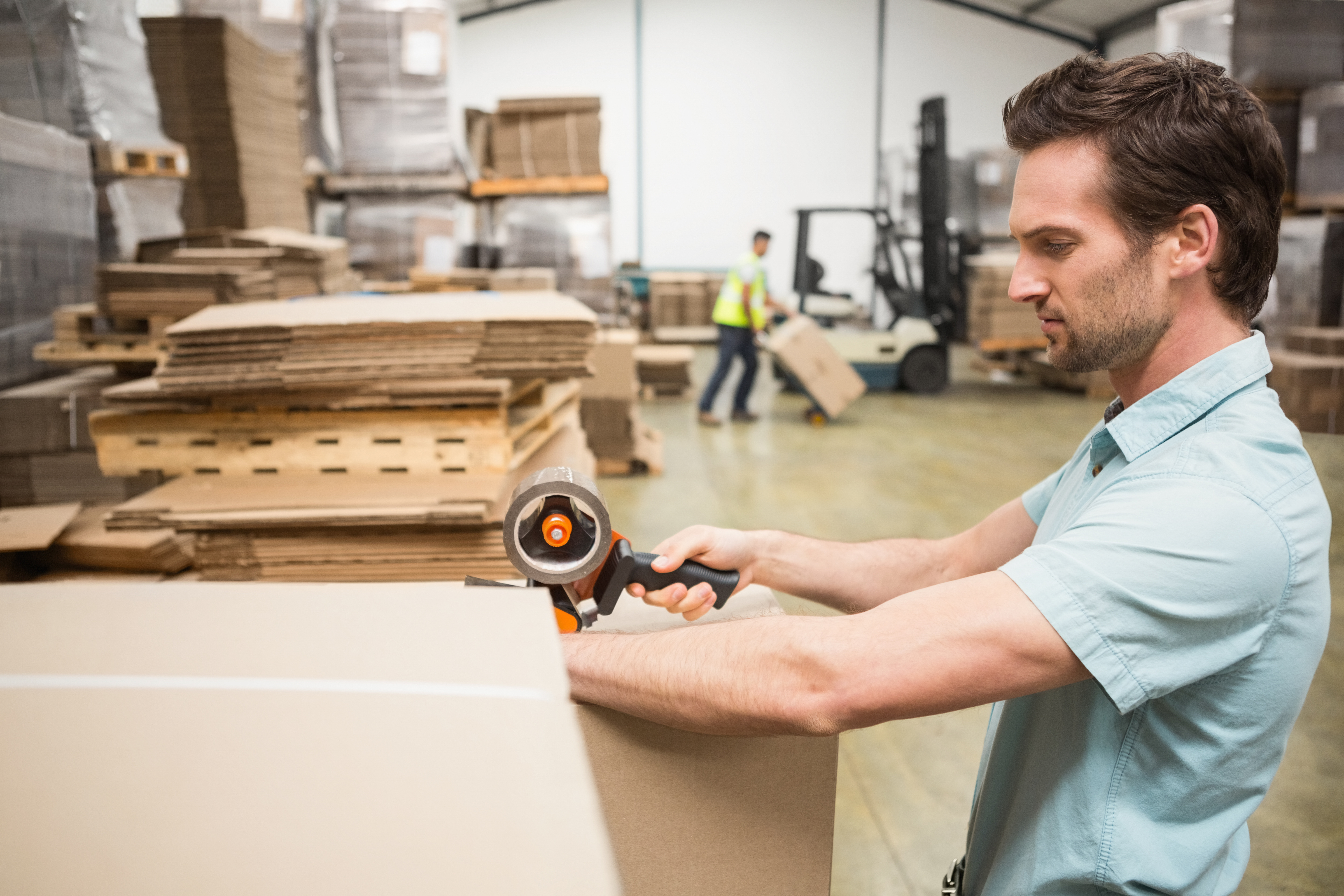 man taping a cardboard box in warehouse
